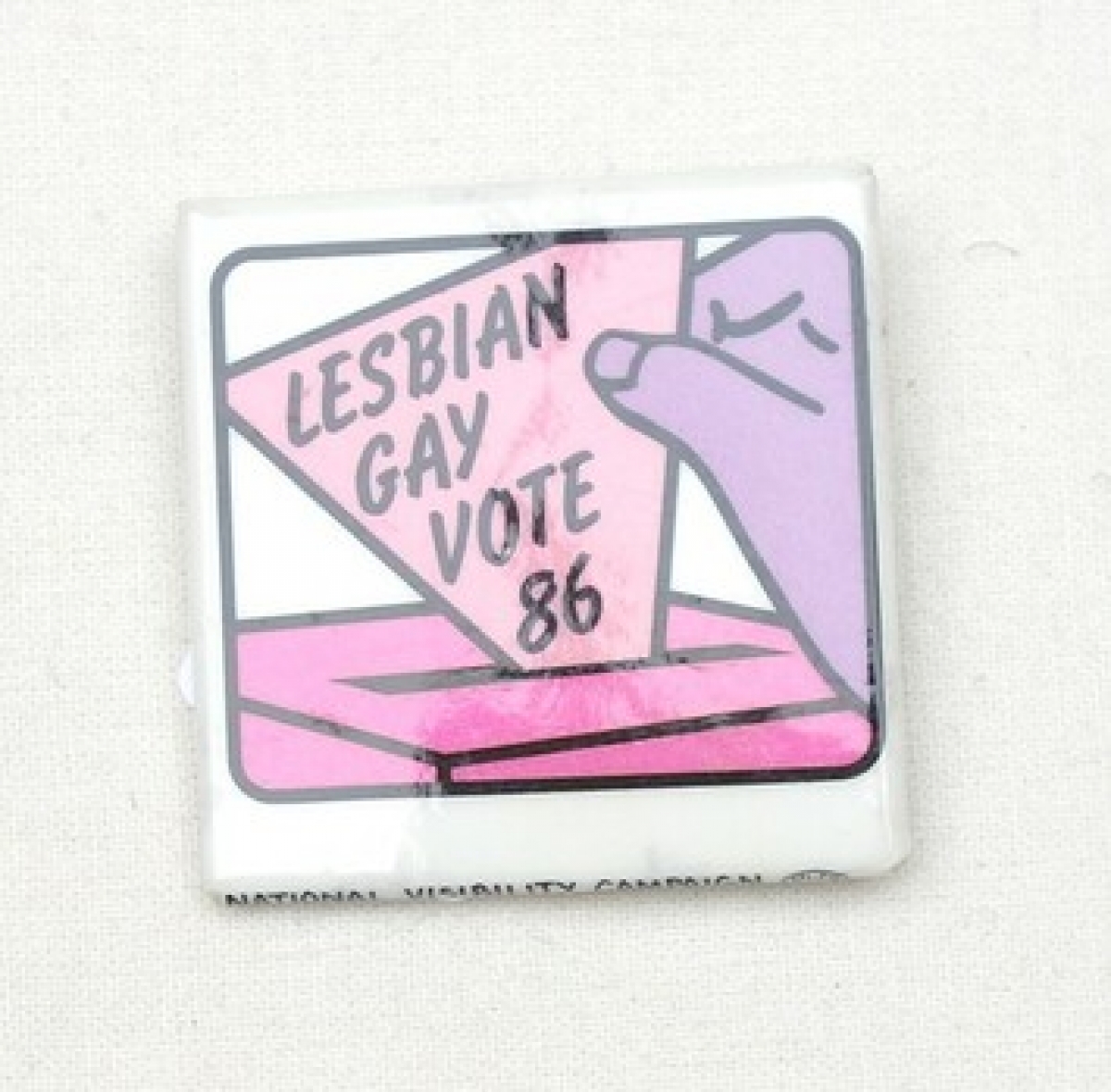 Square badge with a purple hand holding a pink triangle with the text: "LESBIAN GAY VOTE 86". USA, 1986.