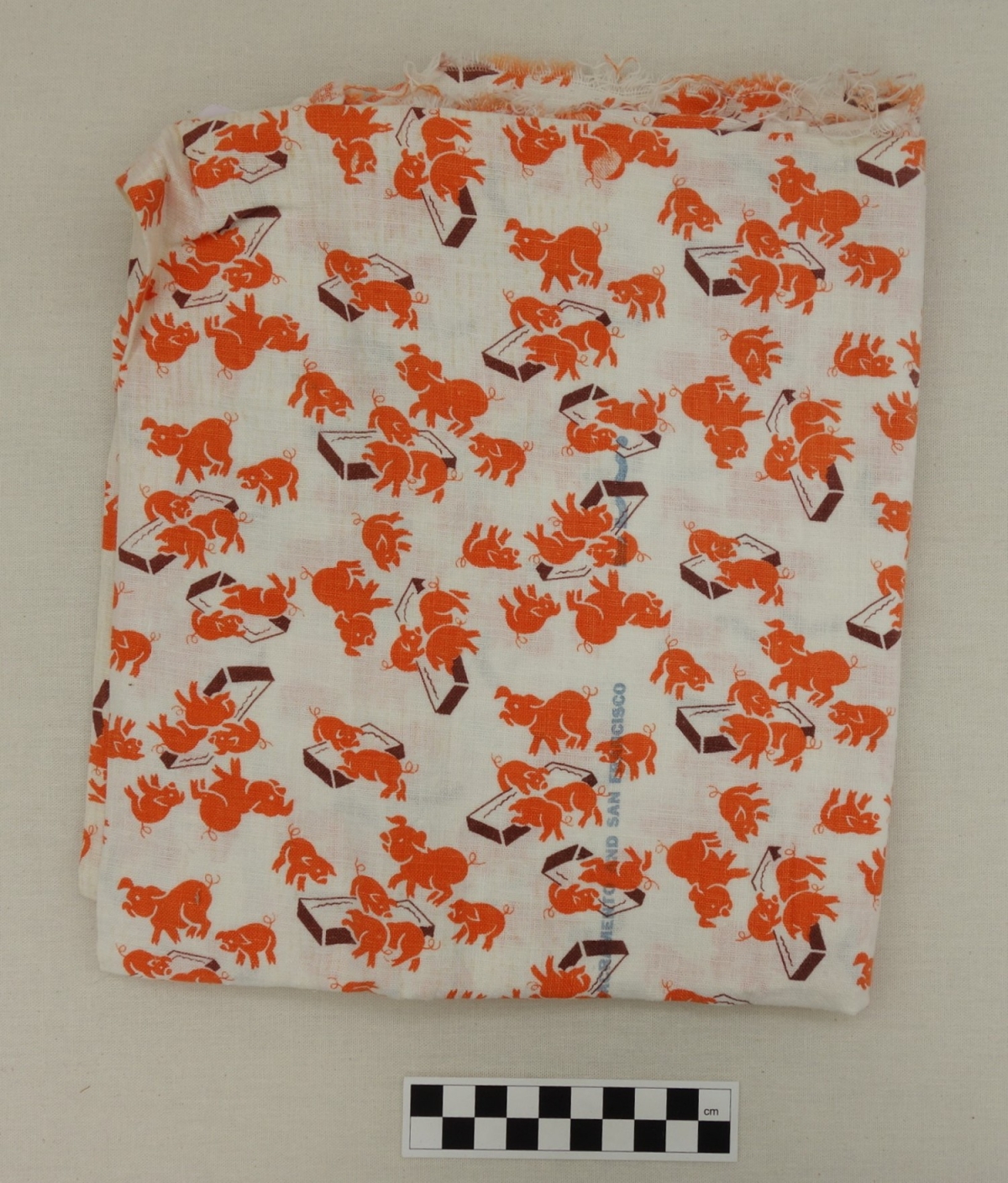 Length of cotton cloth with a design of orange pigs of various sizes eating at brown troughs. USA, mid-1950's (TRC 2017.1366).