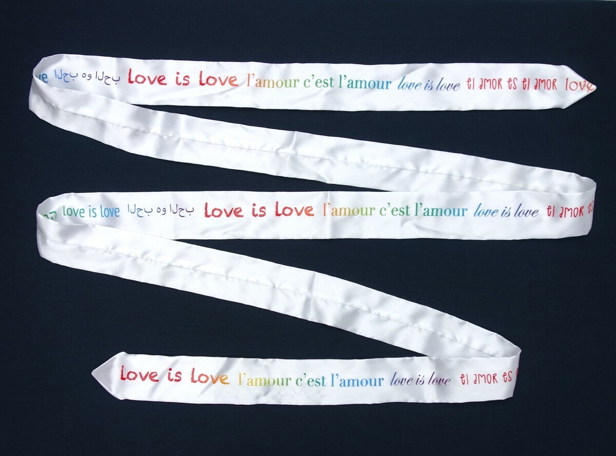 LGBTQ+ tie designed for World Pride 2019, with slogan “Love is love” in six languages, by Ty-Amo. (USA).
