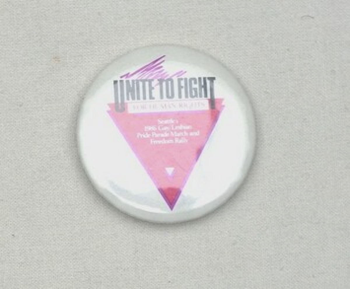 White badge with the text "UNITE TO FIGHT FOR HUMAN RIGHTS &nbsp;SEATTLE&nbsp;1986 GAY/LESBIAN PRIDE PRADE MARCH AND FREEDOM RALLY" over a pink triangle. USA, 1986.