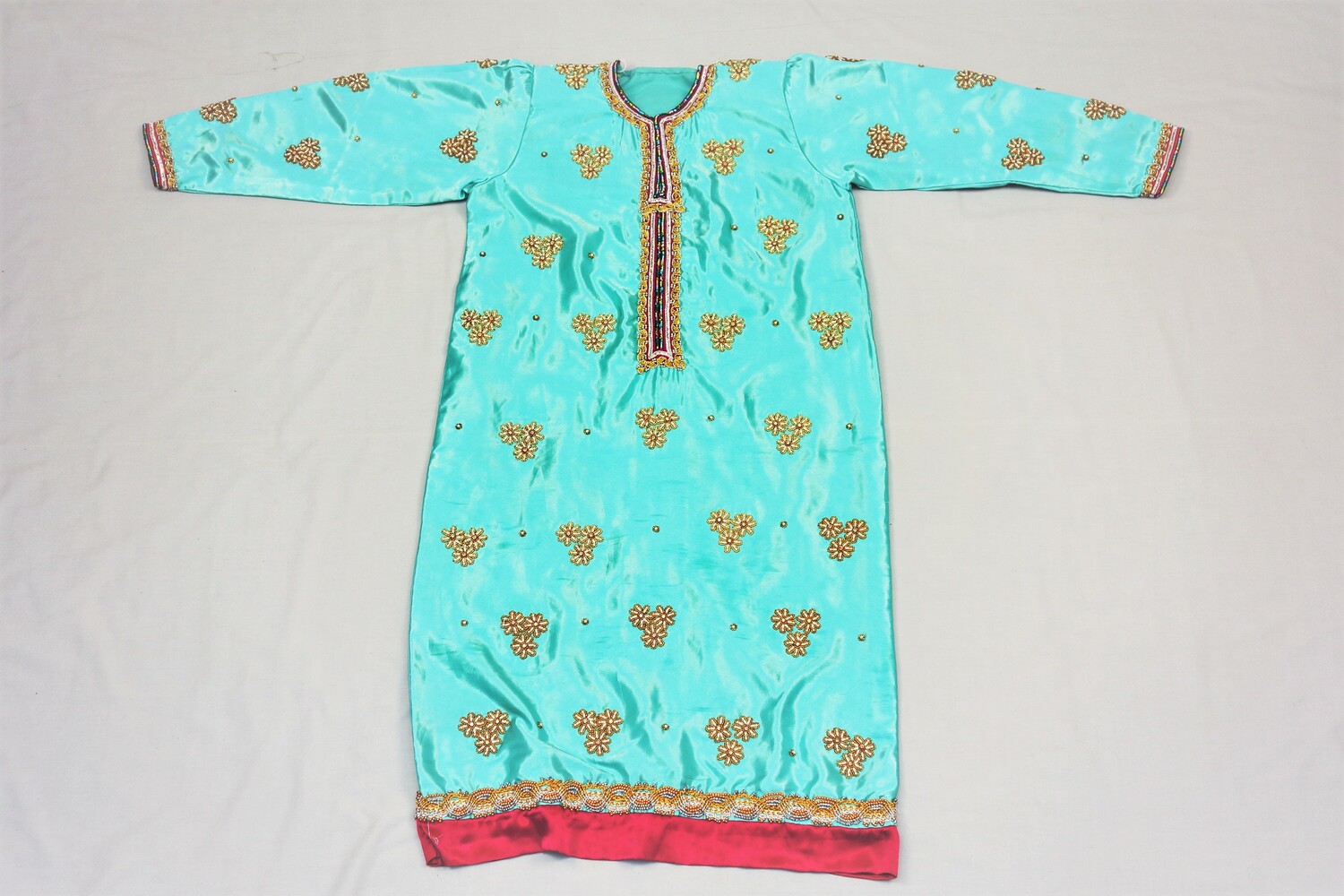 Long dress (tunic) in turquoise satin decorated with metallic thread bands and embellished with fake pearls and diamonds, surrounded by small gold and silver coloured beads. Gift of the Omani Embassy in he Netherlands, 1999 (TRC 1999.0296).