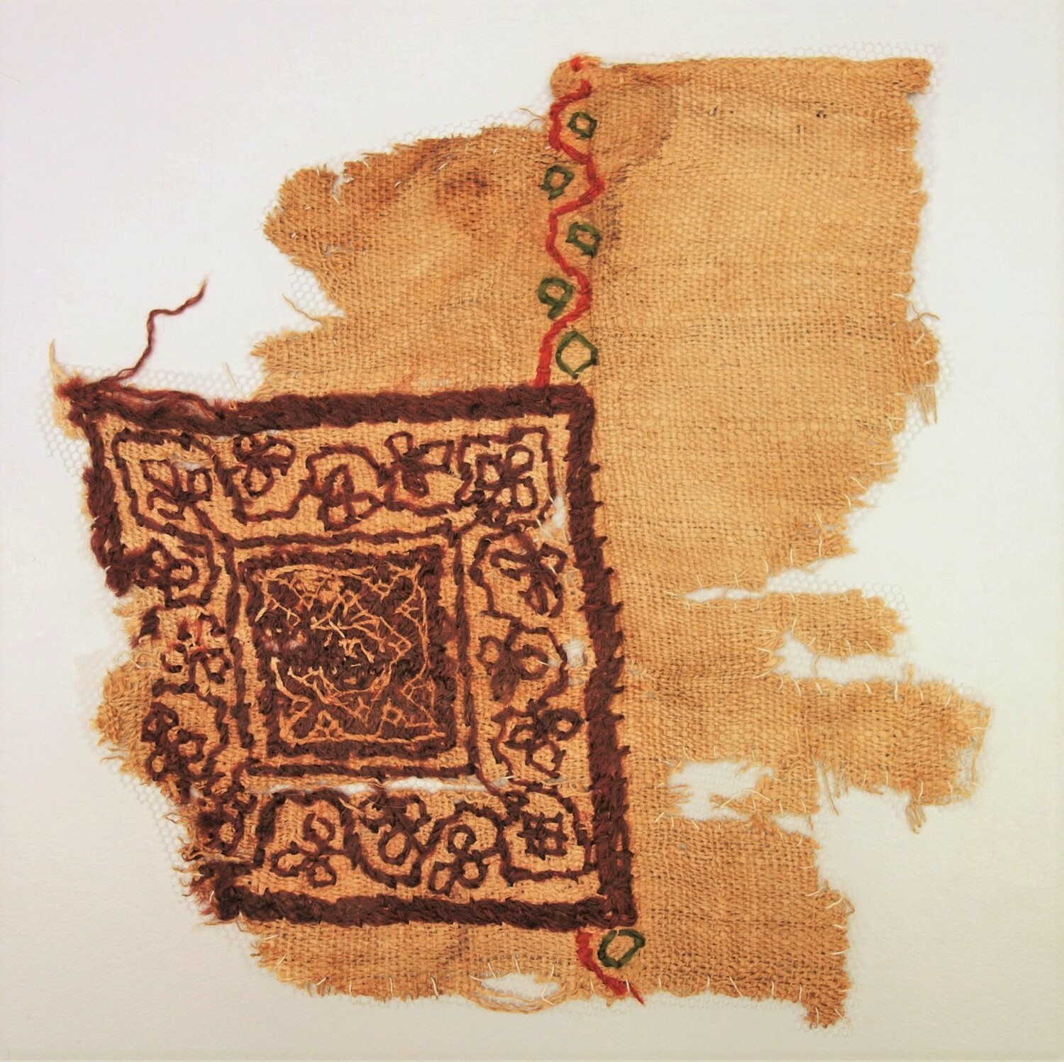Fragment of linen with an embroidered design in red, green and purple wool. Egypt, 5th-6th century AD (TRC 2000.0014). The cloth probably came from a child's tunic that had imitation woven bands and squares typical for Coptic period Egyptian dress.