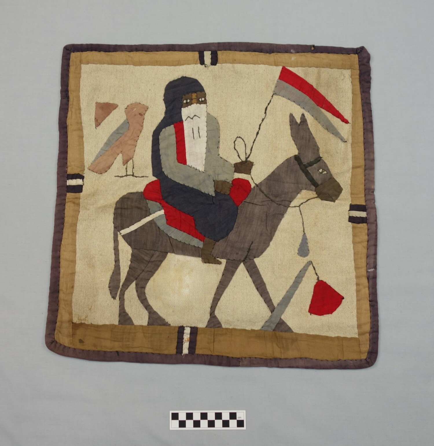 Figure of a woman on a donkey with Ancient Egyptian hieroglyphs in the background. Egypt, Cairo, 1920s, produced for the tourist market (TRC 2015.0560).