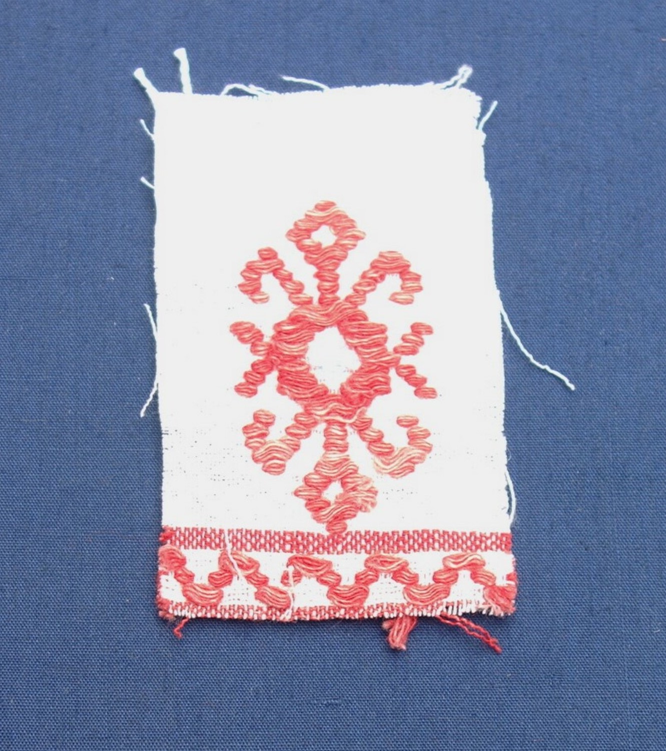 Fig. 2. Sample of cloth with an embroidered design of a mirrored geometric motif in red, and with a narrow zig-zag border (TRC 2019.1677).