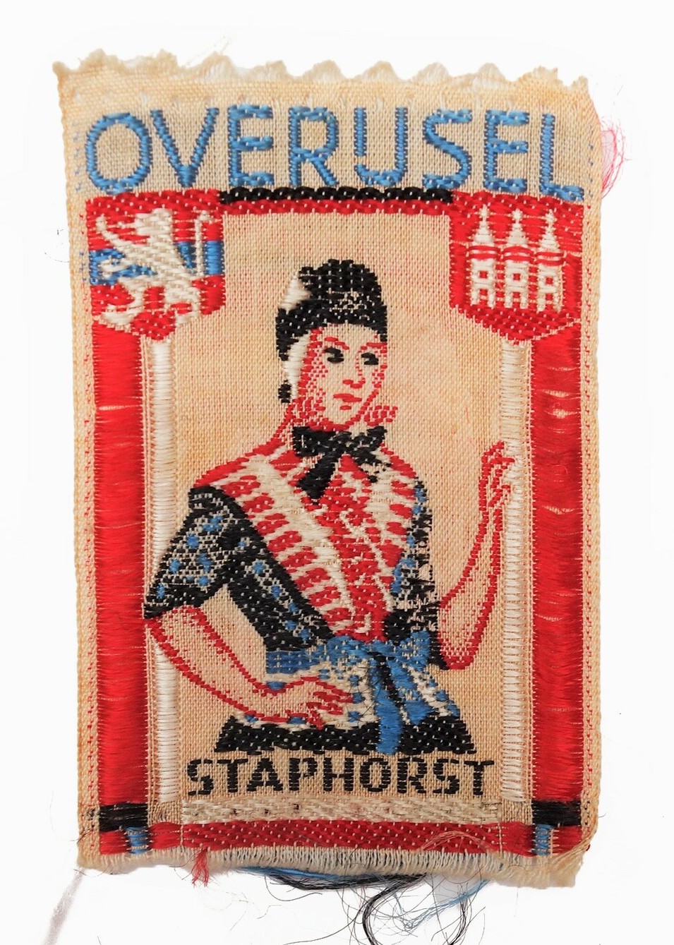 Small cloth badge with a woven design of a Dutch woman in Staphorst regional dress and the name of Overijssel province (misspelt!) with the coat-of-arms of both the province and town (TRC 2021.2018e).