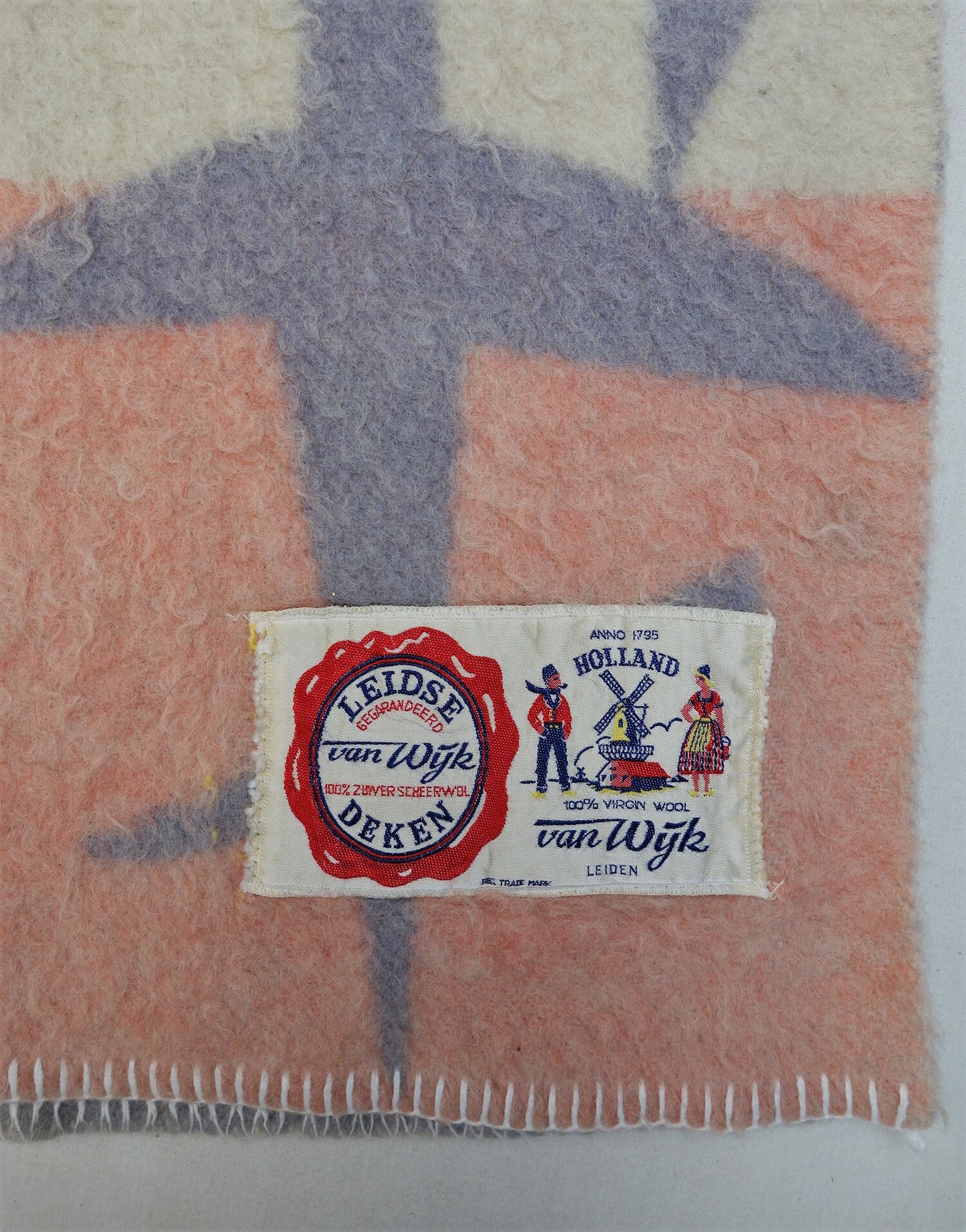 Detail of a woollen blanket produced in Leiden in the 1950s. The label reads: "LEIDSE DEKEN Van Wijk GEGARANDEERD 100% ZUIVERSCHEERWOL" and "ANNO 1795 HOLLAND 100% VIRGIN WOOL VAN WIJK LEIDEN" (TRC 2021.2915).