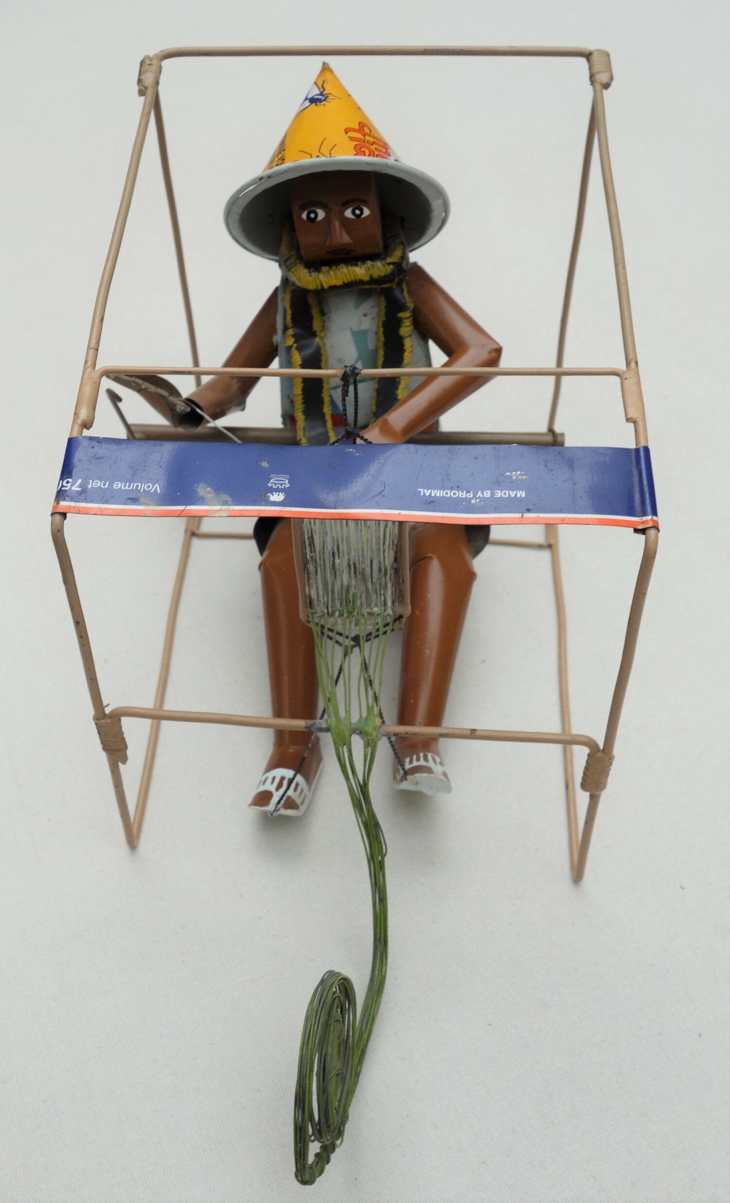 Another photograph of the model of a man working at a frame loom made from old pieces of tin cans and metal strips. Mali, 2004 (TRC 2023.1212).