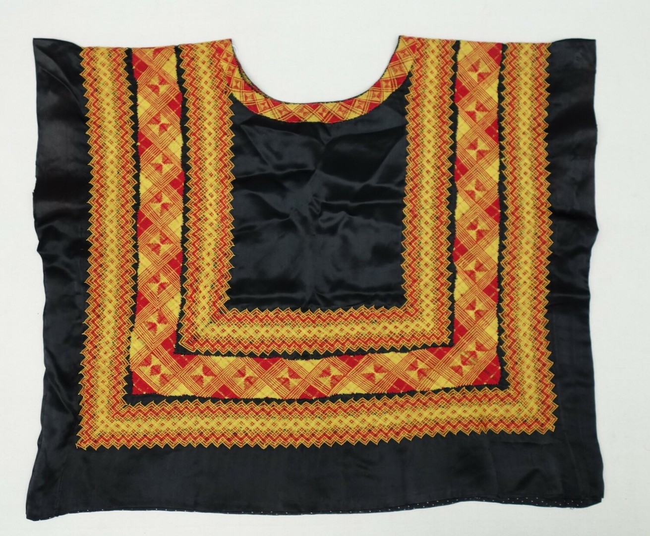 Black satin blouse decorated on the front and back with embroidered bands of repeating geometric and lacy shapes in red and yellow. The garment was known to the Dool family as one of Diane's 'Frida Kahlo' blouses. Antilles, 1950s/1960s (TRC 2023.1218a).
