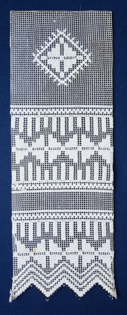Piece of black card with a sample of square network with darned and needle woven patterns using a thick, white thread. Worked by G.H.P. Wening, c. 1922 (TRC 2023.2805.023).