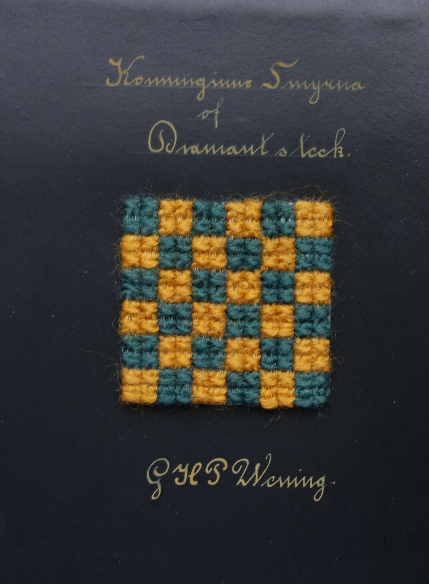 Piece of black card with a sample of white canvas totally covered in a checked pattern of alternating dark blue and orange squares. There is a text: "Koninginne, Smyrna of Diamant steek". Made by G.H.P. Wening between 1919-1922 (TRC 2023.2805.069).
