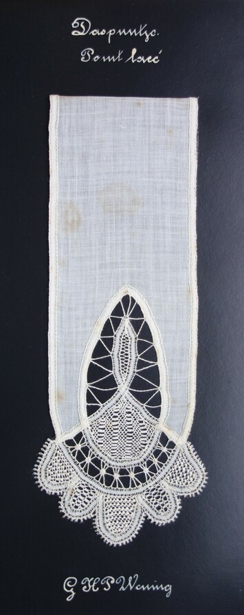 Piece of black card with a sample of white cloth with a cutwork pattern of an oval, waves and pendants, filled with needle lace of various types and patterns. There is a text: "Daspuntje 'point lace' "  Worked by G H P Wening between 1919-192 (TRC 2023.2805.100).