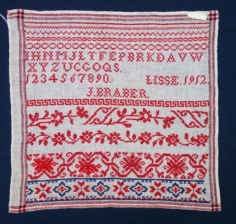 School sampler with lines of repeating geometric and floral motifs, as well as an alphabet, a set of numbers and the text: "LISSE 1912  J. BRABER" (TRC 2023.2906).