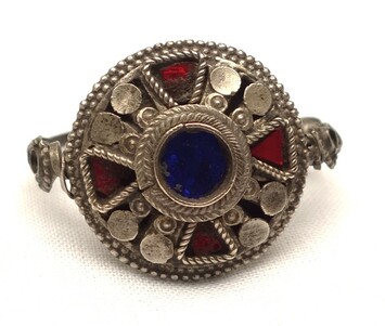 Silver ring with an earring-like opening and a circular front with a blue glass centre, red glass triangles and granulation. Afghanistan, 20th century (TRC 2024.0755).